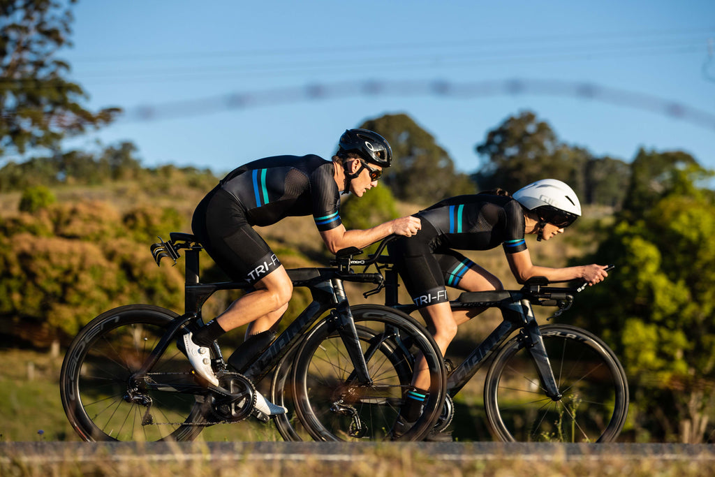 Man and women cycling in the black EVO mens tri suit and womens tri suit on a country road