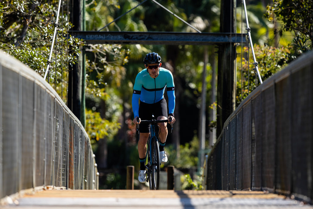 Man cycling across a bridge wearing the mens cycling jersey SYKL pro