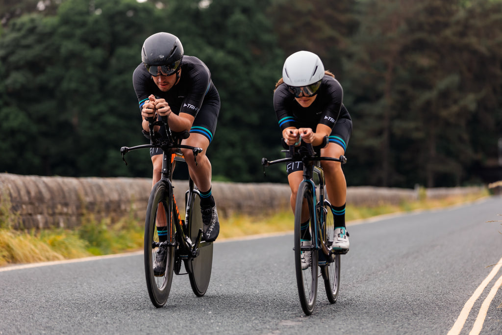 Man and woman cycling along open road wearing black evo mens and womens tri suit