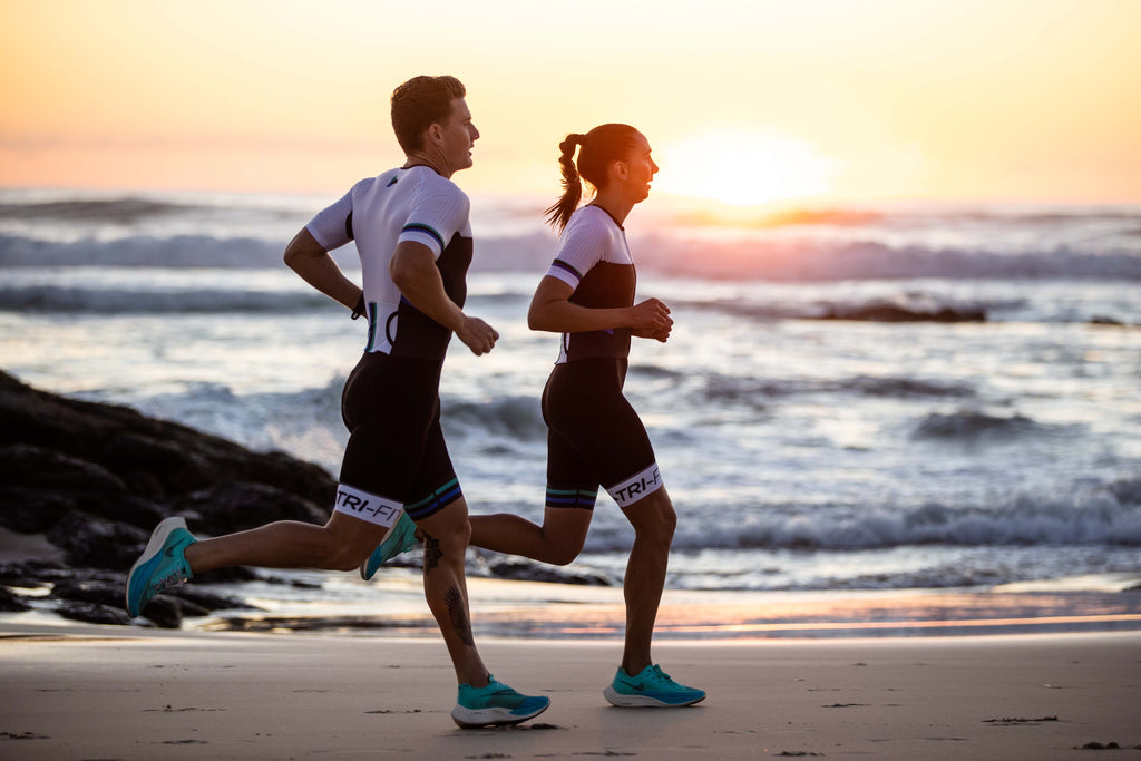 man and women running along the beach wearing the evo mens and womens tri suits with sunset in the background