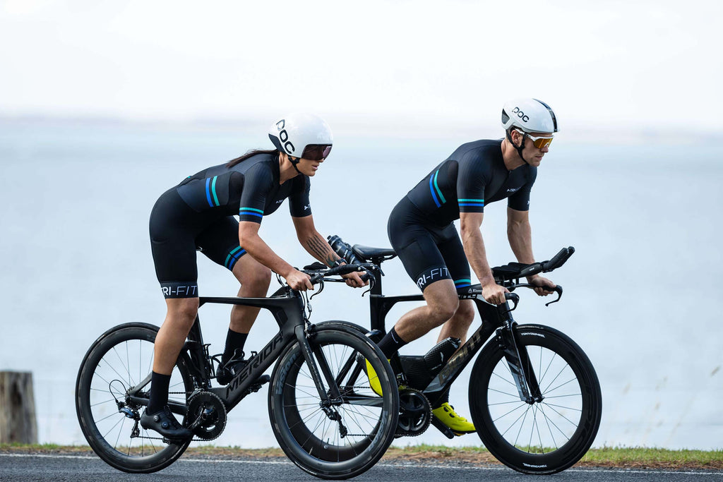 Man and woman cycling along the seafront in the EVO black tri suit